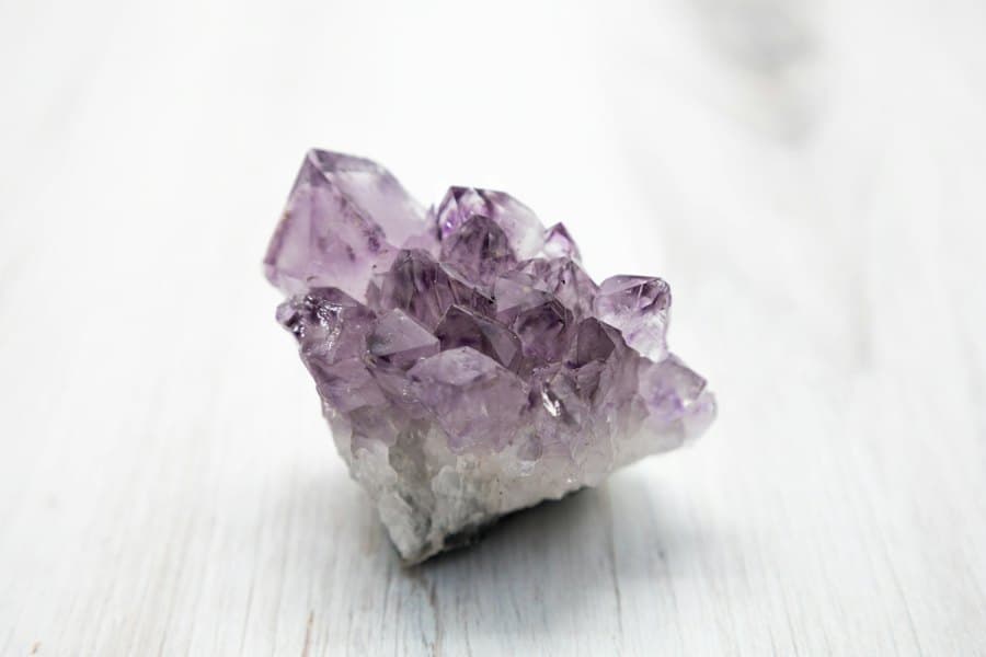 A single small amethyst cluster on pale wood, lit as if being inspected